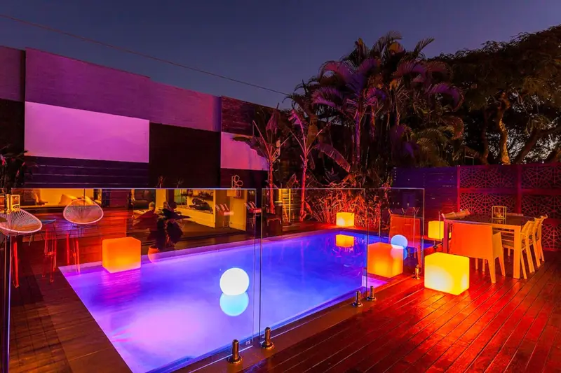 Saltwater pool lit with colour at night, with glowing cube seats on the deck