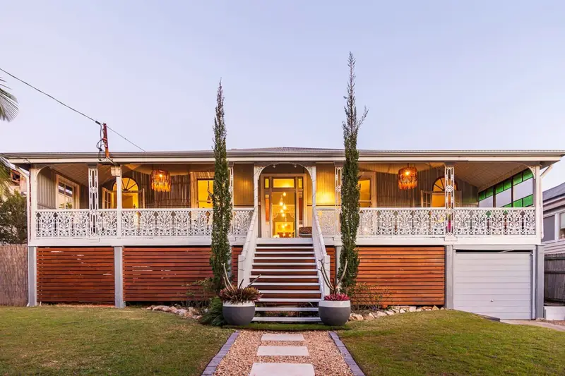 White Queenslander at dusk with cast-iron lacework verandah and lit interiors