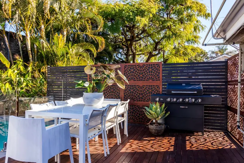 Outdoor dining table and barbecue on the timber deck beside the pool