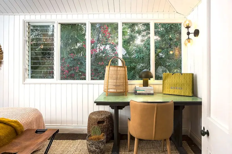 Study nook with a desk and lamp beneath windows onto the tropical garden