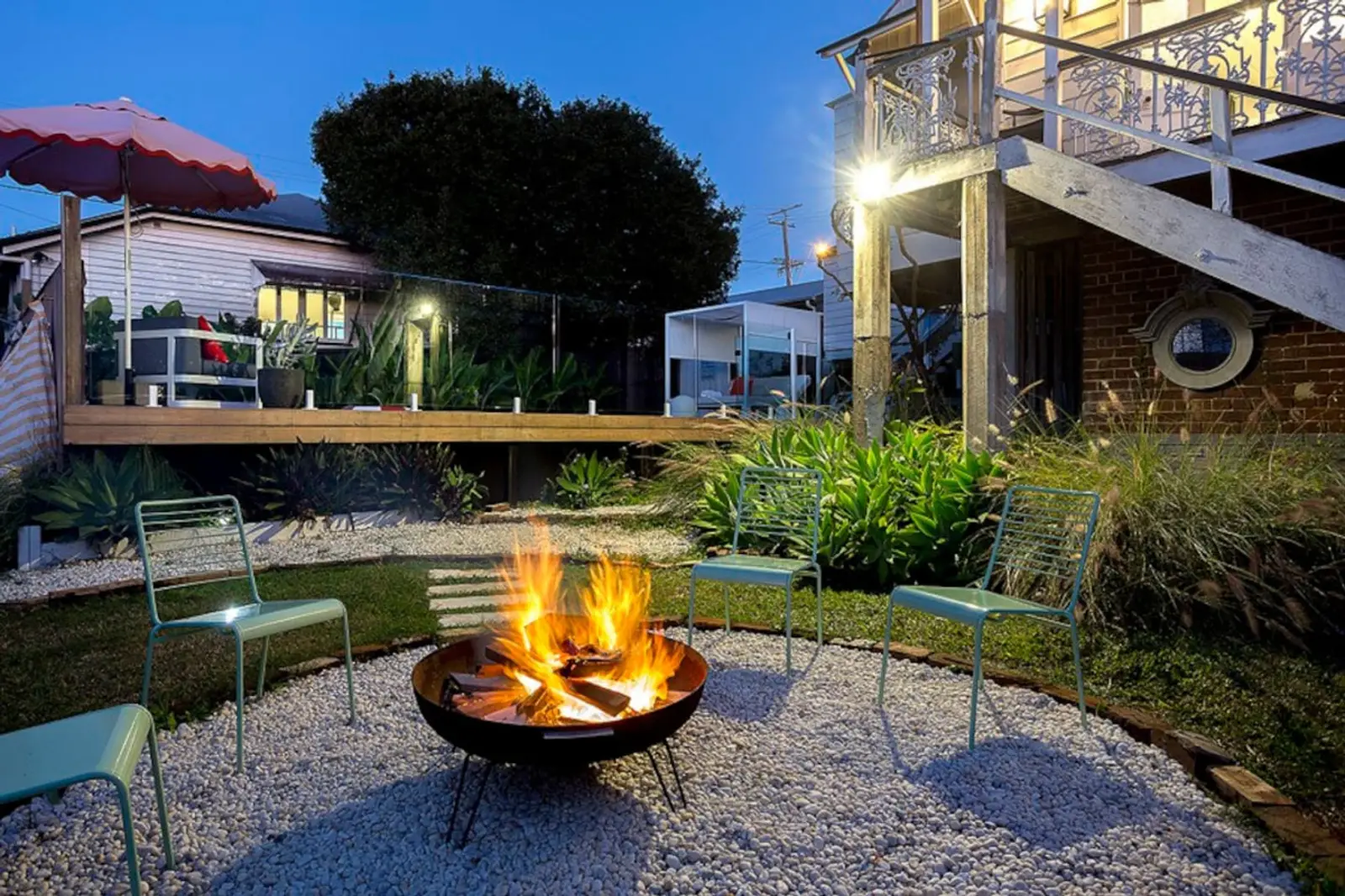 Fire pit ringed with chairs in the garden at dusk, the mansion lit behind