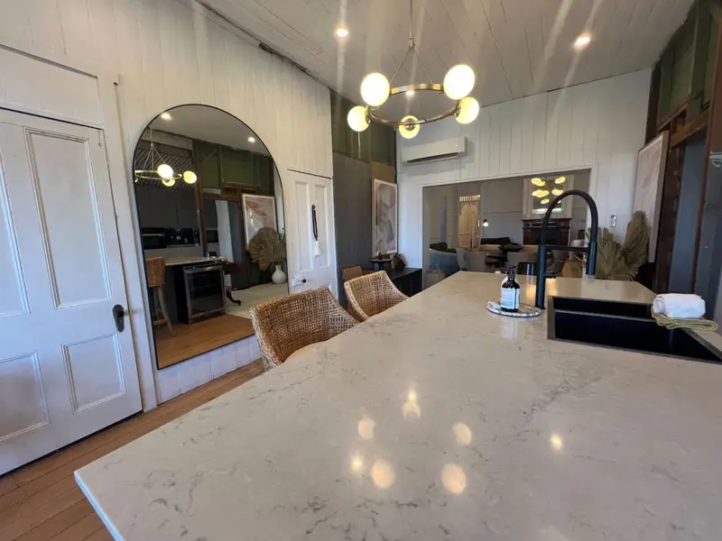 Kitchen island in white marble under a brass chandelier, with an arched mirror