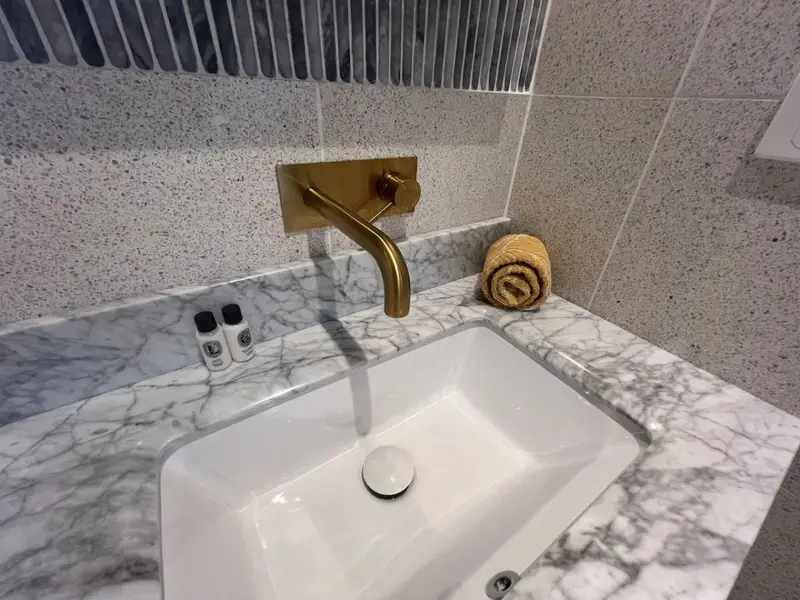 Brass wall-mounted tap over a marble basin