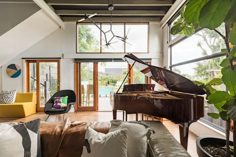 Vaulted living room with a grand piano and glass doors opening to the pool deck