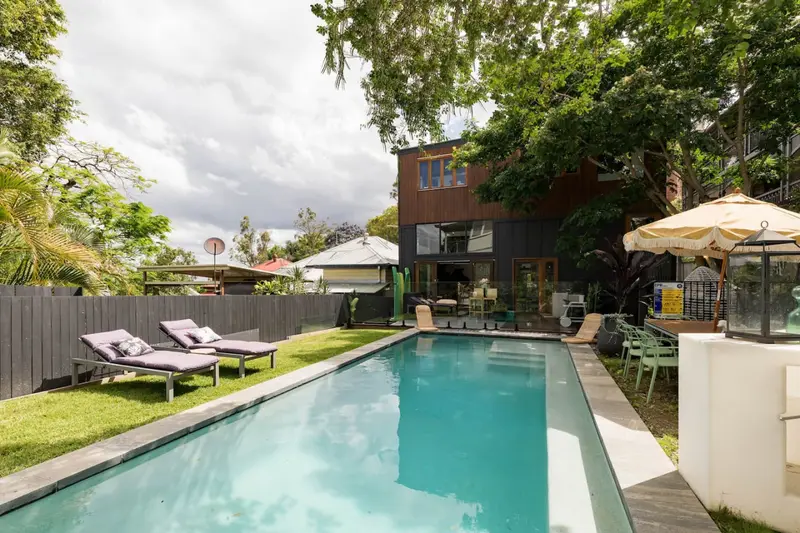 Lap pool with sun loungers on the lawn and the dark timber house behind