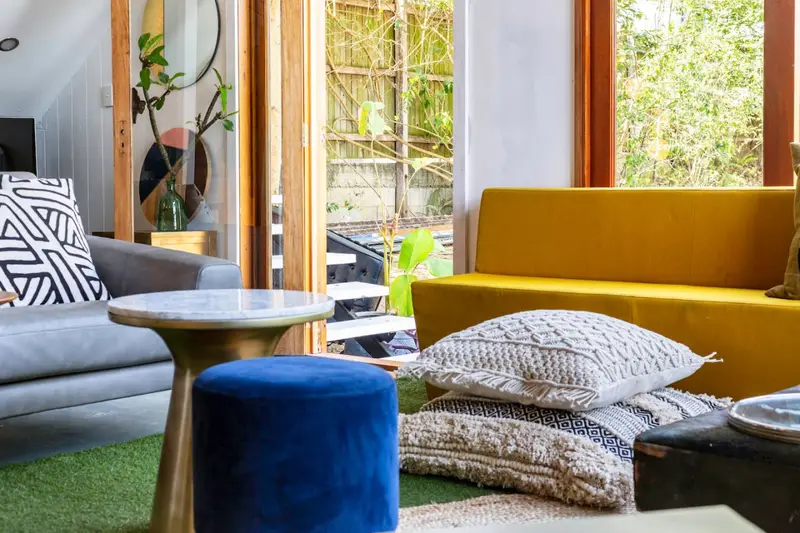 Sitting area with a mustard velvet bench, floor cushions and open doors to the garden