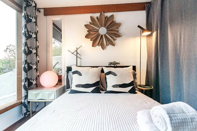 Bedroom with a sunburst mirror, patterned curtains and a window over the treetops