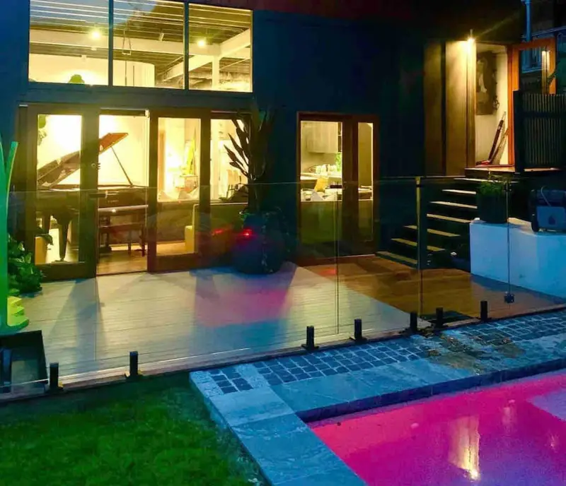 The house and pool lit at night, with the piano visible through the glass doors
