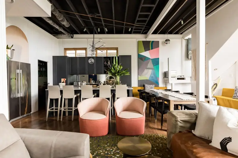 Open-plan kitchen and dining room under black steel beams, with bar stools and a long timber table