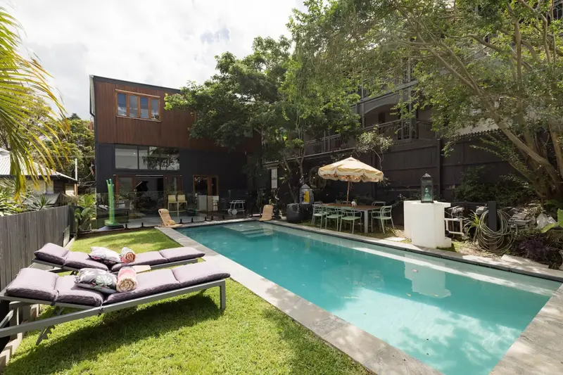 Lap pool at midday, framed by palms and the two-storey timber house