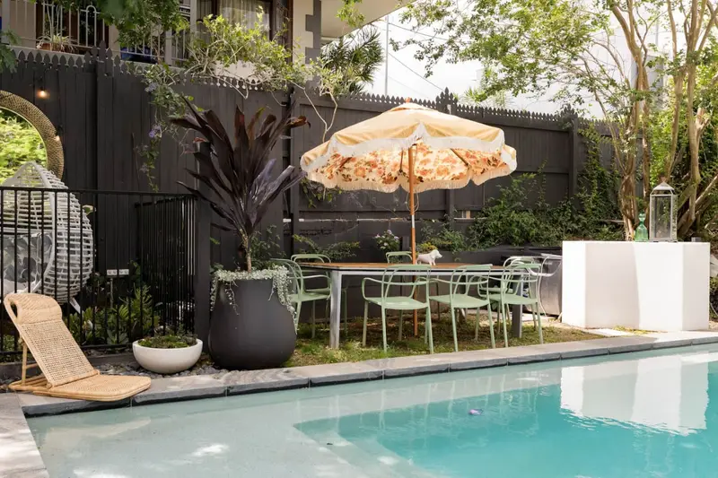 Poolside dining table under a fringed umbrella beside planted borders
