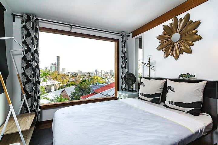 Bedroom with a large window framing the city skyline and rooftops